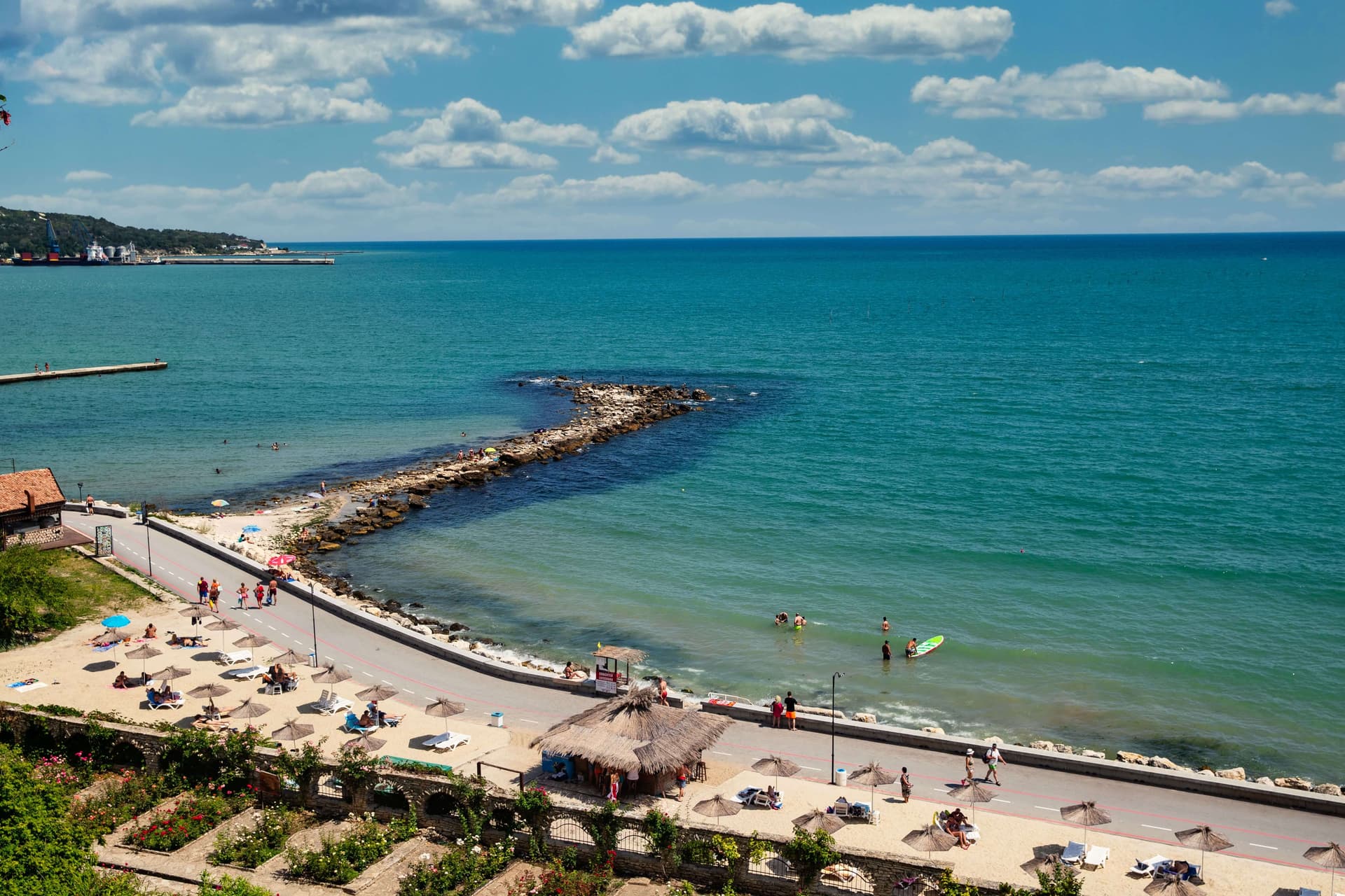 Balchik's narrow strip of sand and thatched parasols beside the seafront road, seen from above
