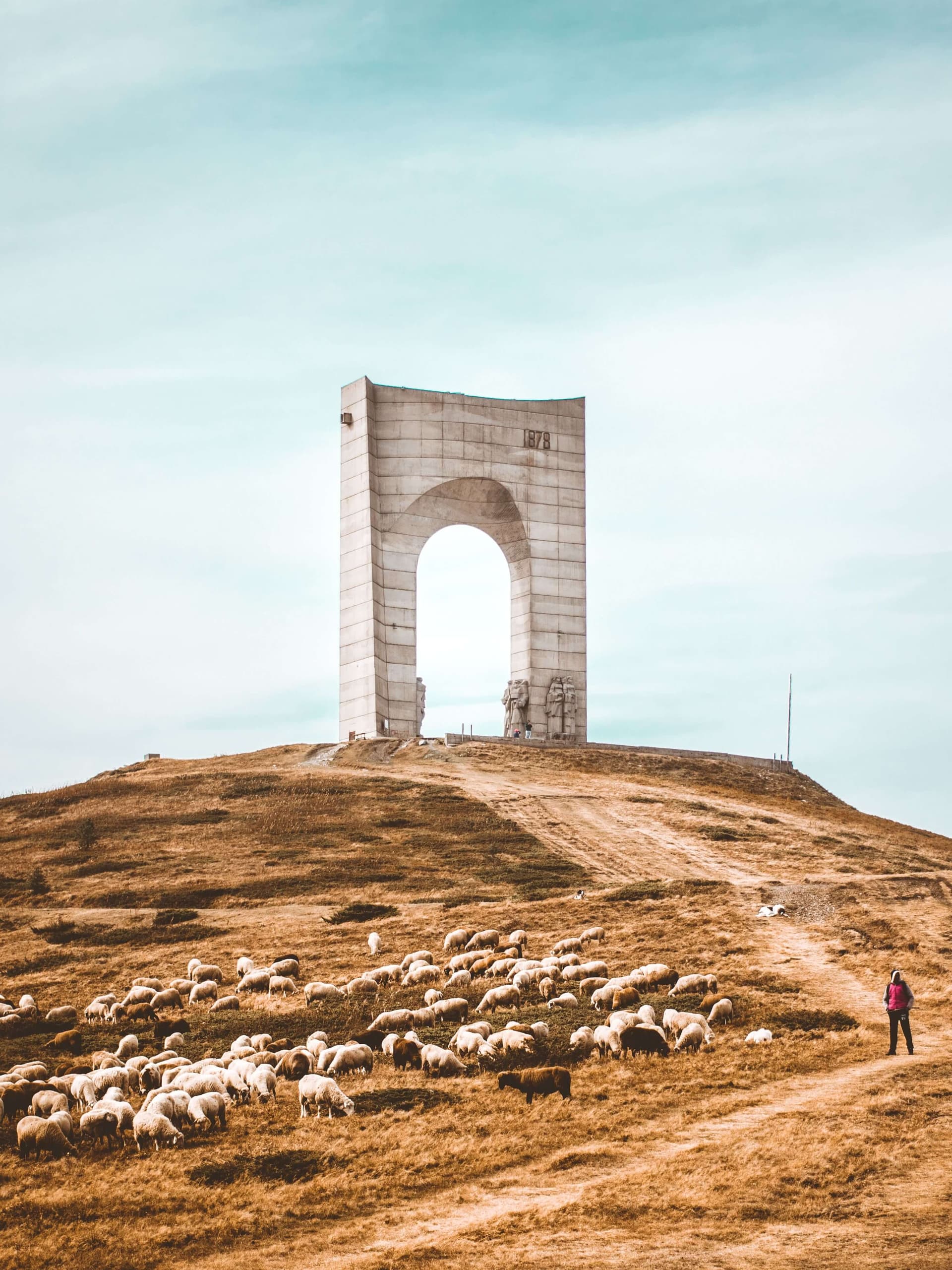 The Arch of Freedom monument on the Troyan Pass at Beklemeto, with a flock grazing on the open ridge below it