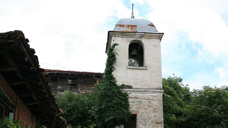 The stone bell tower of the church in Svezhen, next to a collapsing timber house