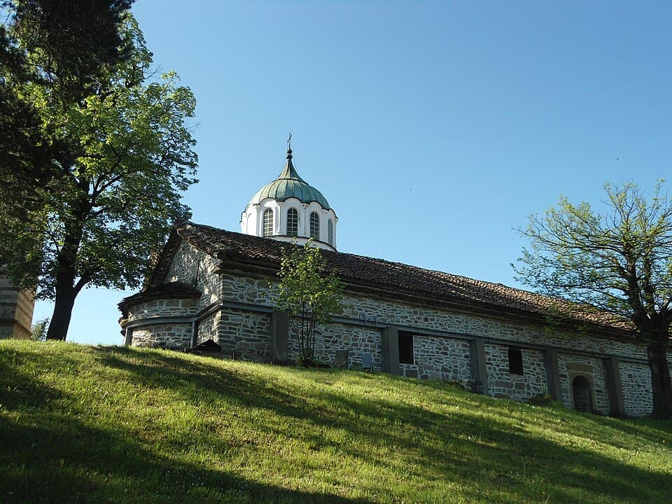The stone Church of St Nicholas with its green dome on a grassy slope in Elena
